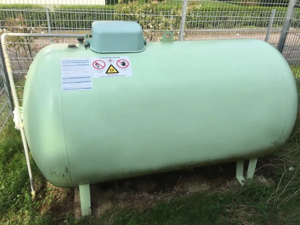 Hellgrüner oberirdischer Flüssiggastank mit Sicherheitskennzeichnung, eingezäunt im Garten