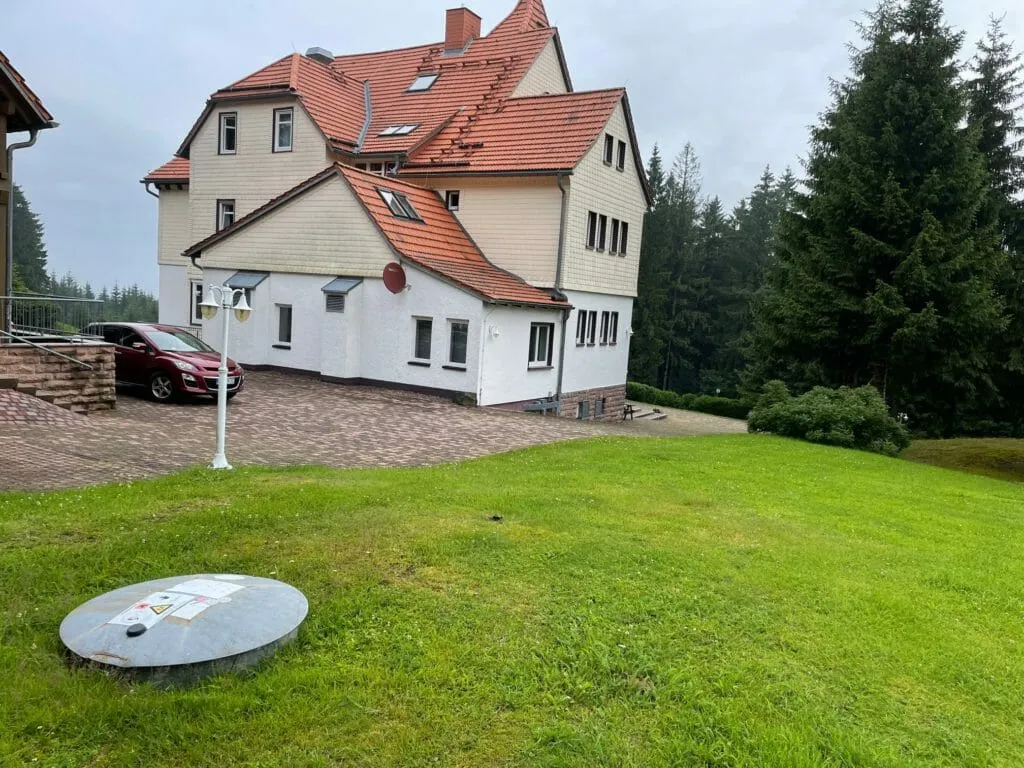 Domschachtdeckel eines unterirdischen Flüssiggastanks auf einer Wiese vor einem Haus